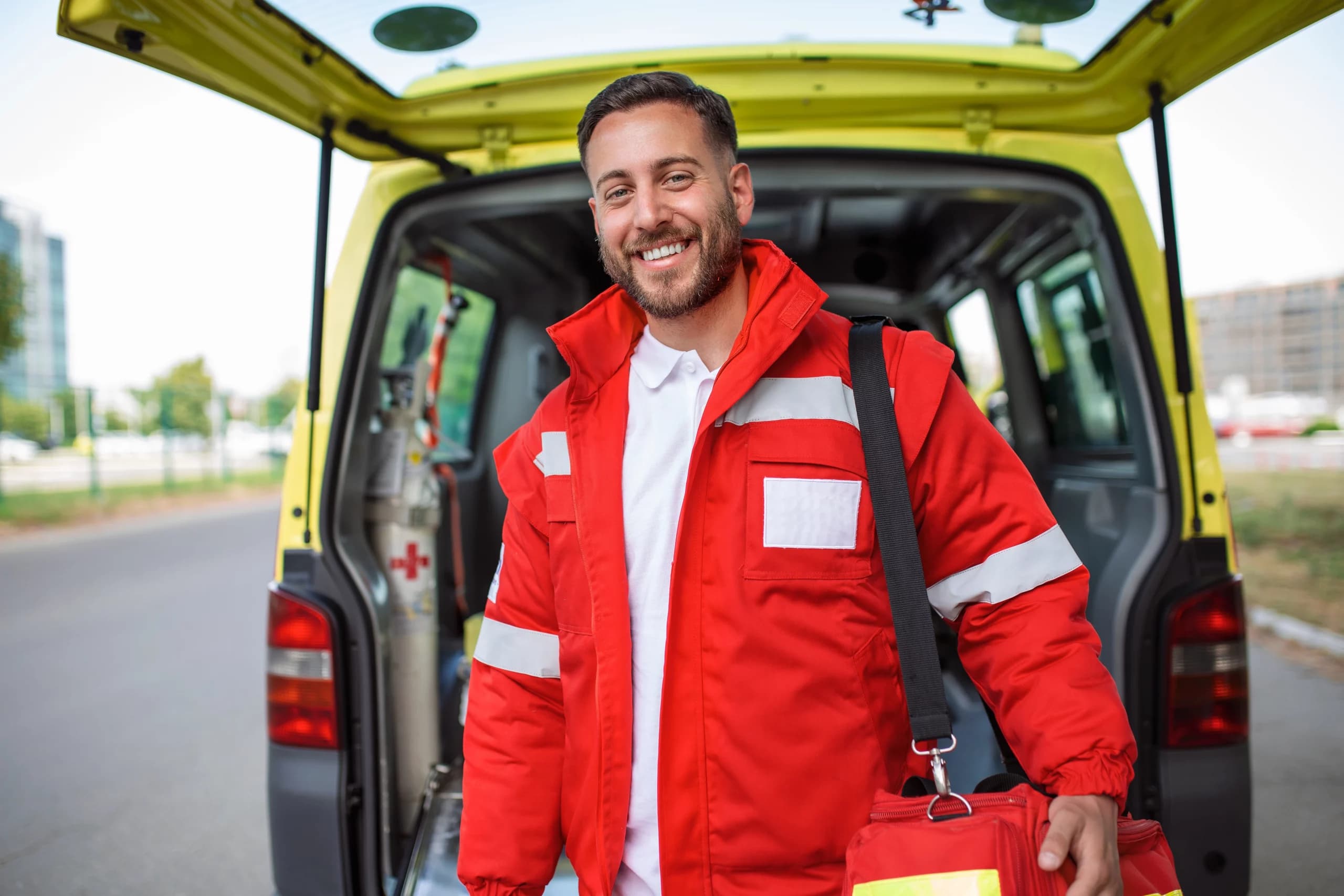Secouriste souriant en tenue professionnelle devant une ambulance, symbole de la formation Qualiopi en secourisme.